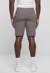 Shorts cargo gris avec une taille élastique, des poches latérales et un ourlet cousu, vus de l'arrière. Tissu texturé et coupe décontractée.