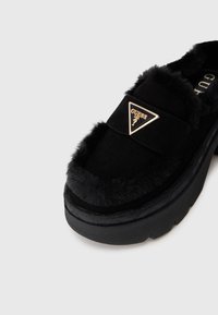 Sorte ruskinds slip-on sko med faux fur kant, tyk platformsål og en triangel logo-plade med guldfarvede detaljer.