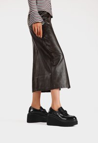 Scarpe platform nere con una finitura lucida e liscia, abbinate a una gonna midi in pelle marrone, caratterizzata da un design elegante e una texture sottile.