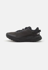 Chaussure de sport noire avec une tige en mesh, un collier rembourré et une semelle en caoutchouc. Présente un design texturé et un logo au niveau du talon. Construction légère.