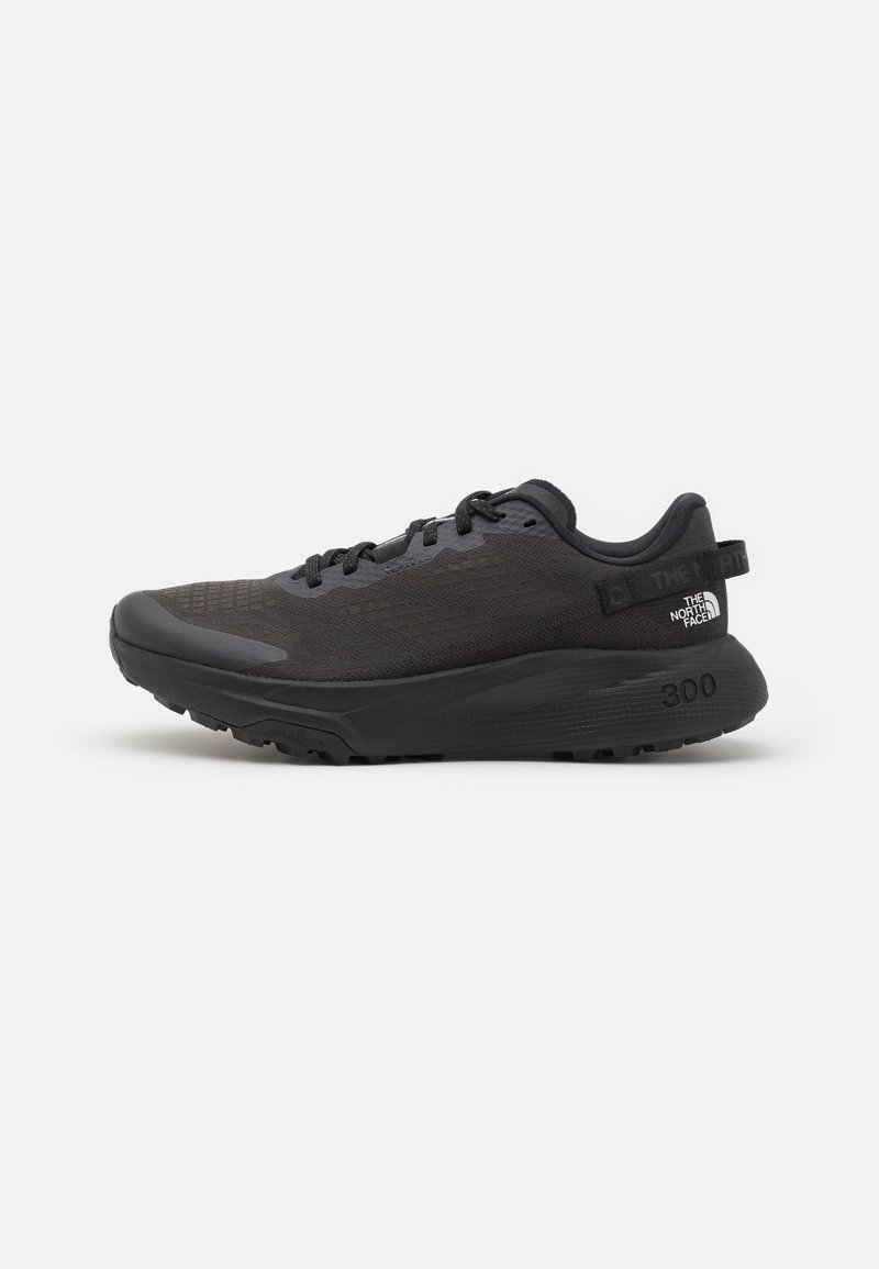 Chaussure de sport noire avec une tige en mesh, un collier rembourré et une semelle en caoutchouc. Présente un design texturé et un logo au niveau du talon. Construction légère.