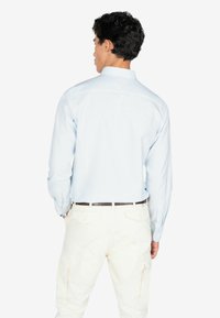 Lichtblauw geruit shirt met lange mouwen, overhemdkraag en witte broek met zakken, gezien vanaf de achterkant.