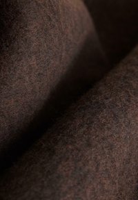 Tessuto di feltro marrone con una texture morbida, caratterizzato da un motivo marmorizzato e una superficie liscia, presentato in pieghe.