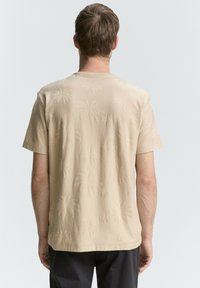 Tricou bej cu un model texturat de palmieri, mâneci scurte și guler rotund. Material neted cu o croială lejeră.