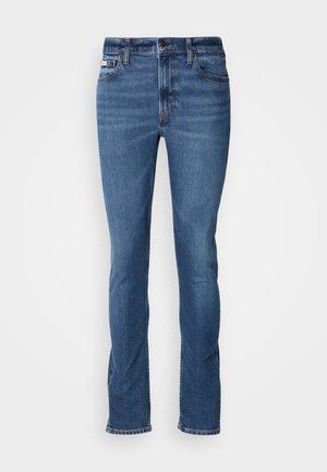 Blue denim jeans featuring a straight leg, five-pocket design, contrast stitching, and a button-fly closure. Light fading near the knees.