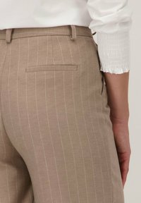 Beige streepjasje met een achterzak, gemaakt van textuurstof. Gecombineerd met een wit shirt met een gerimpeld mouwdetail.