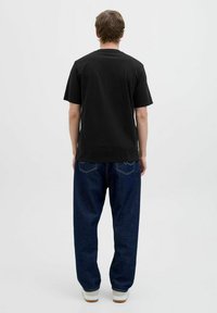 Schwarzes Baumwoll-T-Shirt mit kurzen Ärmeln, kombiniert mit lockeren, dunkelblauen Jeans. Die Jeans verfügen über ein klassisches Fünf-Taschen-Design.