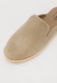 Bežīgas slip-on kurpes, kas izgatavotas no mīkstas zamšādas, ar noapaļotu purngalu un jutu virvju apdari uz zolēm. Minimālistisks dizains, plakanā profila.