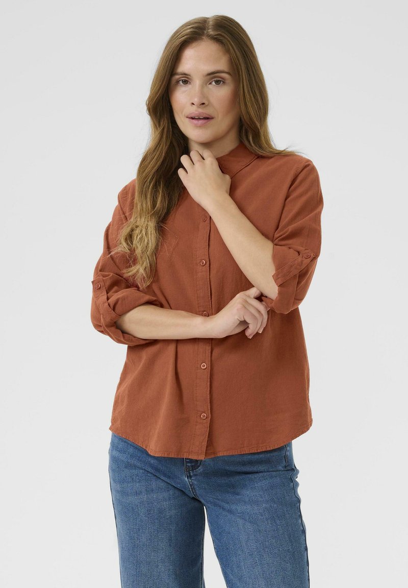 Roestkleurig overhemd met opgerolde mouwen, lichtgewicht stof en een kraag. Draagt met blauwe denim jeans. Eenvoudig en casual ontwerp.