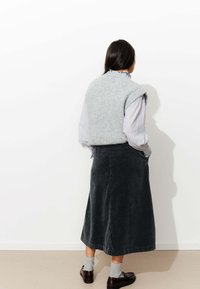 Gilet en laine gris sur une chemise à rayures claires, associé à une jupe midi en velours côtelé noir. Les accessoires comprennent des chaussettes grises et des chaussures marron.