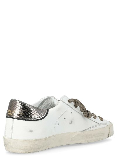 Baskets en cuir blanc avec des accents en texture reptilienne métallique, des lacets marron texturés et une semelle légèrement usée. Présente un logo de la marque sur le talon.