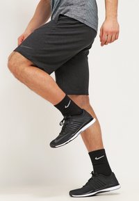 Cortos deportivos negros hechos de un tejido ligero, con una textura suave y un logo sutil en la parte frontal. Combinados con zapatillas de correr negras y calcetines.
