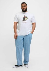 Camiseta blanca de algodón con un gráfico de un esqueleto en motocicleta, combinada con pantalones de mezclilla azul claro y zapatillas negras.