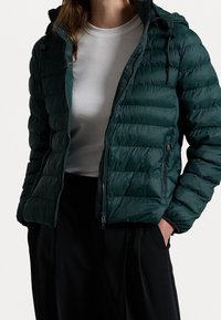 Veste en duvet verte avec un devant zippé, une capuche et des poignets élastiques ; fabriquée à partir d'un matériau brillant et matelassé avec des côtes horizontales.