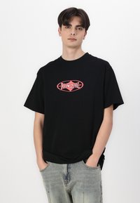 Svart bomull T-skjorte med en rød "Rip Curl" logo i midten, med avslappet passform og korte ermer. Kombinert med slitte jeans.