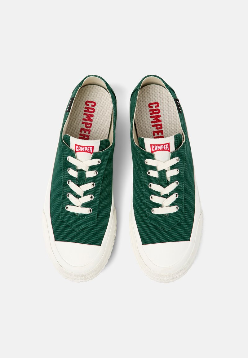 Sneakers in tela verde con suola in gomma bianca. Presentano un design con lacci e sei fori per i lacci, e un logo rosso "CAMPER" sulla linguetta.