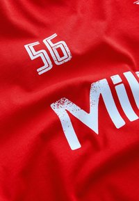 Czerwona koszulka sportowa z numerem "56" i białym napisem "Mil...", z zniszczonym efektem na literach.