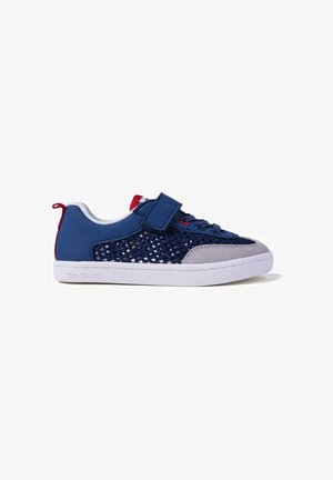 Zapatilla azul marino con paneles laterales de malla, puntera de ante gris, tira de velcro y suela de goma blanca con detalles en rojo.