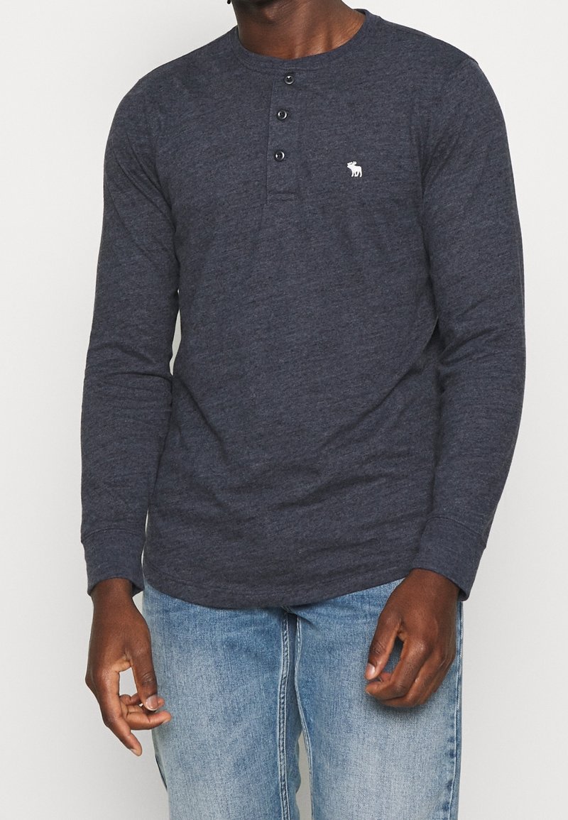 Námořnická dlouhá rukávová košile henley vyrobená z měkké látky, s třemi knoflíky na límci a malým logem na levém hrudi.