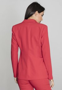Czerwony marynarka dopasowana z wyraźnymi ramionami, gładkiego materiału i eleganckim tyłem. Posiada klapowy kołnierz i dopasowany krój.