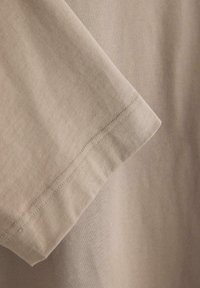 Beige kortærmet t-shirt i bomuld med synligt dobbeltsyet kantdetalje på glat stofbaggrund.