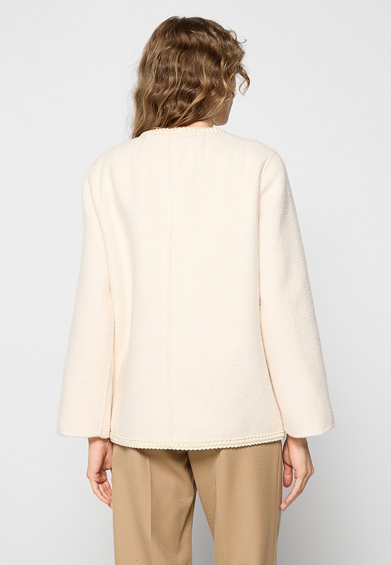 Cremfarbener Wolljacke mit geradem Schnitt, weiten Ärmeln und strukturiertem Finish. Mit einer gewellten Kante am Saum verziert.