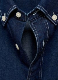 Temno modra denim srajca z usnato ovratnico, belimi gumbi in kontrastnimi šivi. Odprta na vratu, razkriva notranjo teksturo.