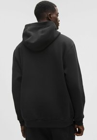 Fekete kapucnis pulóver puha, texturált anyagból, nagy kapucnival és bordázott ujjak és alj részletekkel. Egyszerű dizájn, nincs látható logó vagy minta.