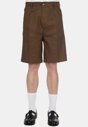 Pantaloncini marroni da uomo fino al ginocchio abbinati a calzini bianchi e scarpe nere intrecciate in pelle con fibbia su sfondo bianco.