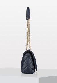 Navy blue quilted leather handbag with gold chain strap and leather shoulder pad, shown from side on white surface and background.