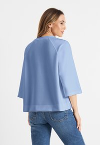 Lichtblauwe sweatshirt met een boxy pasvorm, wijde driekwart mouwen en gladde stof. Heeft een ronde halslijn en een rechte zoom.