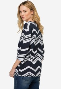 Volný námořnický top se vzorem šipky v bílé barvě. Tričko má tříčtvrteční rukávy a kulatý výstřih.