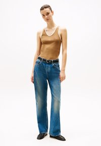 Débardeur marron avec des finitions blanches, associé à un jean large bleu avec une texture décolorée. Accessoirisé avec une ceinture noire et des chaussures.