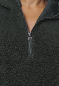 Pullover in pile verde scuro con colletto alto, fronte con mezza zip, superficie testurizzata e morbida. Chiusura con zip argentata a metà.