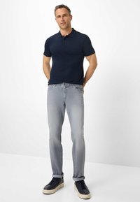 Herren Polohemd in Marineblau kombiniert mit hellgrauen Jeans und schwarzen Sneakers. Lässiger Schnitt mit klassischem Kragen und dezenter Textur.