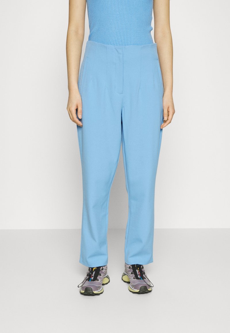 Pantalon bleu clair à la texture lisse, doté d'une taille haute et d'une coupe droite. Associé à des chaussures de sport grises.