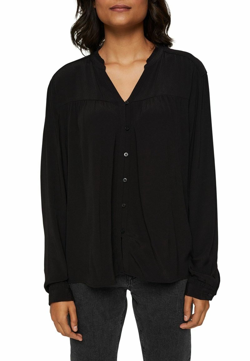 Blouse noire à manches longues avec un col en V, des boutons à l'avant et une coupe décontractée. Présente une texture lisse et un éclat subtil. Sans motifs ni embellissements.