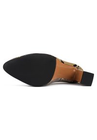 Chaussure à talon haut à bout pointu avec semelle texturée noire et dessus à motif peau de serpent, vue par le dessous.