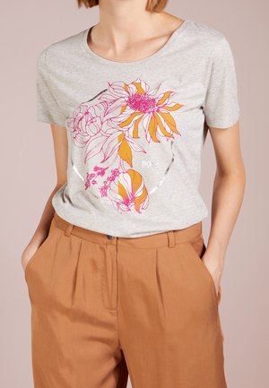 Szara bawełniana koszulka z kolorowym kwiatowym motywem w odcieniach różu i pomarańczy, okrągły dekolt, krótki rękaw, w połączeniu z brązowymi spodniami.