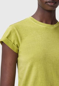 Zielona bawełniana koszulka z krótkimi, podwiniętymi rękawami i okrągłym dekoltem. Miękka w dotyku, nieco spłowiała, z widocznymi detalami szwów.