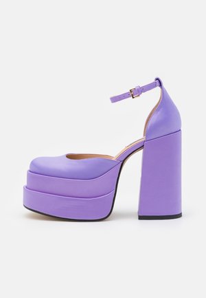 Talons de plateforme violets avec un talon bloc épais et une lanière à la cheville. Matériau lisse et mat avec un bout arrondi et un design de plateforme superposée.