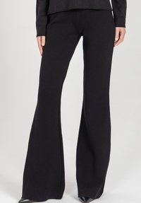 Czarne spodnie z rozszerzaną nogawką wykonane z miękkiego materiału, charakteryzujące się gładką fakturą i dopasowanym w pasie krojem. Projekt rozszerza się do szerokiego rozszerzenia na dole.