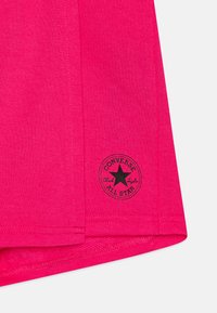 T-shirt en coton rose à manches courtes avec un patch logo Converse noir et un détail en tissu texturé à l'ourlet.