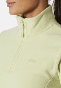 Jasnożółty polarowy pulower z pół zamkiem, wysokim kołnierzem i wytłaczanym logo. Miękka tekstura i bezszwowe detale konstrukcyjne.