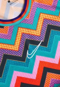 Nærbillede af et flerfarvet stof med zigzag-mønster og en hvid Nike-logo samt en rund halsudskæring med blå, orange og røde striber.