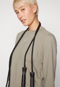 Felpa verde con scollo rotondo e piccolo logo bianco. Corda per saltare nera appesa al collo, con impugnature nere testurizzate.