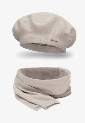 Berretto a maglia beige con un motivo testurizzato e un piccolo dettaglio di marca, abbinato a una sciarpa a maglia beige coordinata, anch'essa testurizzata.