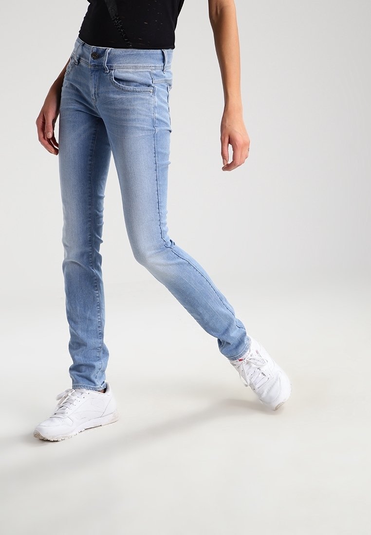 Světle modré skinny džíny se zesvětleným vzhledem, obsahující pět kapes a zipový rozkrok. Model má na sobě bílé tenisky, které zvýrazňují fitted design džínů.