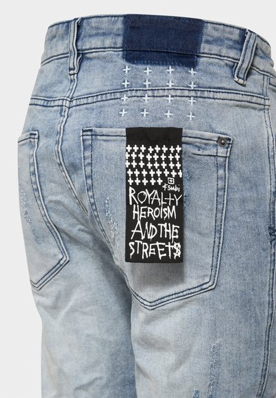 Hellblaue Jeans aus Denim mit Distressed-Textur, ausgestattet mit einem schwarzen Etikett auf der Gesäßtasche, das weiße Schriftzüge und grafische Akzente aufweist.