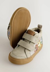Beige High-Top-Sneaker verfügen über zwei Klettverschlüsse, Gummisohlen mit strukturiertem Profil und illustrierten Cartoon-Charakteren an den Seiten.